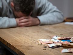 Ein Mann hat seinen Kopf auf seine Hände gelegt, vor ihm liegen Geldscheine, Münzen und Bankkarten auf dem Tisch (Foto: picture alliance/dpa | Hannes P Albert)