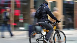 Ein Radfahrer fährt mit Kopfhörern durch eine Fußgängerzone  (Foto: picture alliance / dpa | Emily Wabitsch)